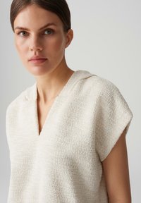 Cream textured top with a V-neck and short sleeves, featuring a casual design and soft, woven fabric.