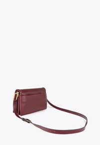Burgundská kožená kabelka přes rameno s měkkou texturou, která má dlouhý popruh a elegantní, minimalistický design.