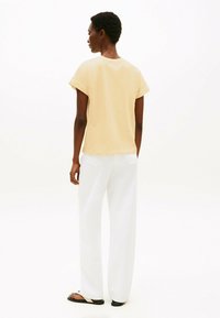 T-shirt giallo chiaro a maniche corte con risvolti, abbinato a pantaloni bianchi larghi e sandali neri, visto da dietro.