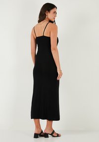 Black spaghetti strap maxi dress with a fitted silhouette, smooth texture, and a straight hemline. Worn with black block heel sandals.