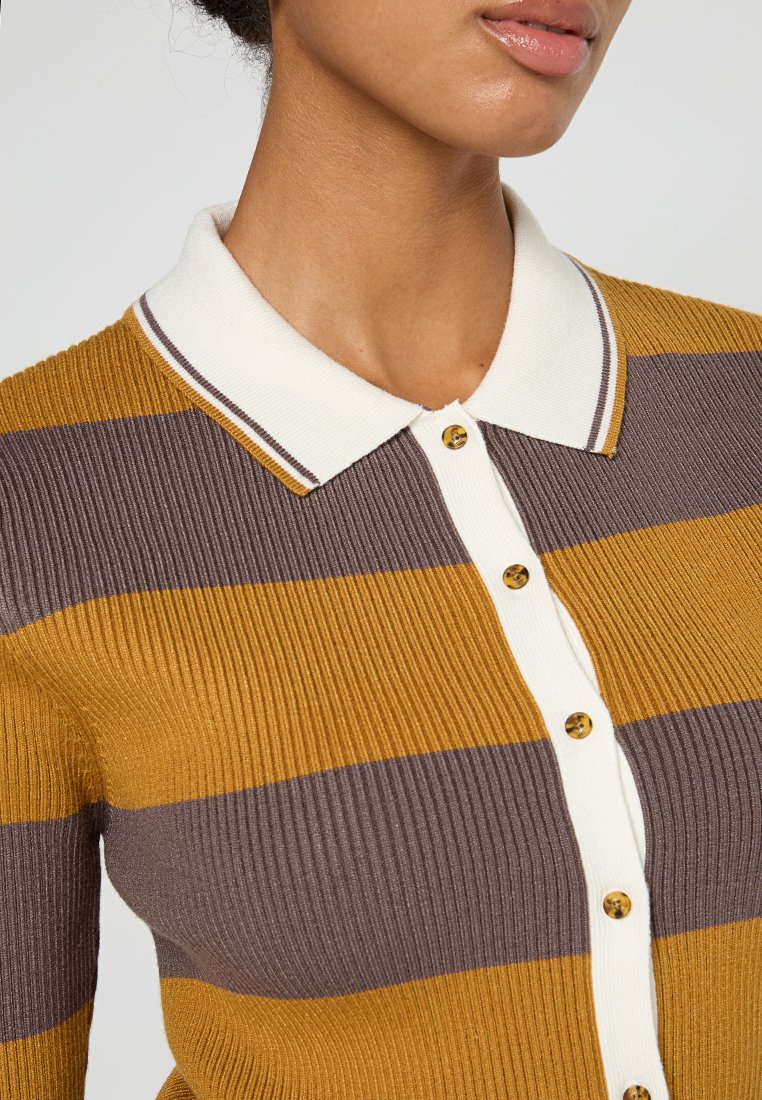 Cárdigan acanalado con rayas horizontales mostaza y marrón, que presenta un cuello blanco con solapas, cinco botones dorados y una tela texturizada.
