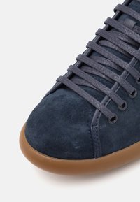 Sneaker in suede blu navy con punta tonda, superficie testurizzata e suola in gomma marrone a contrasto; allacciata con lacci piatti blu scuro abbinati.