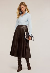 Lichtblauwe button-up shirt, bruine geplooide leren rok, getextureerde bruin slangenprint hakken en een kleine handtas in meerdere kleuren.