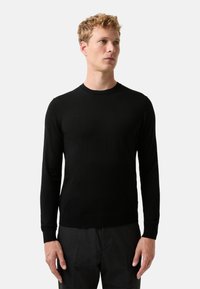 Czarny sweter z długim rękawem wykonany z miękkiego materiału, z okrągłym dekoltem i ściągaczami na rękawach, gładka struktura bez widocznych wzorów.