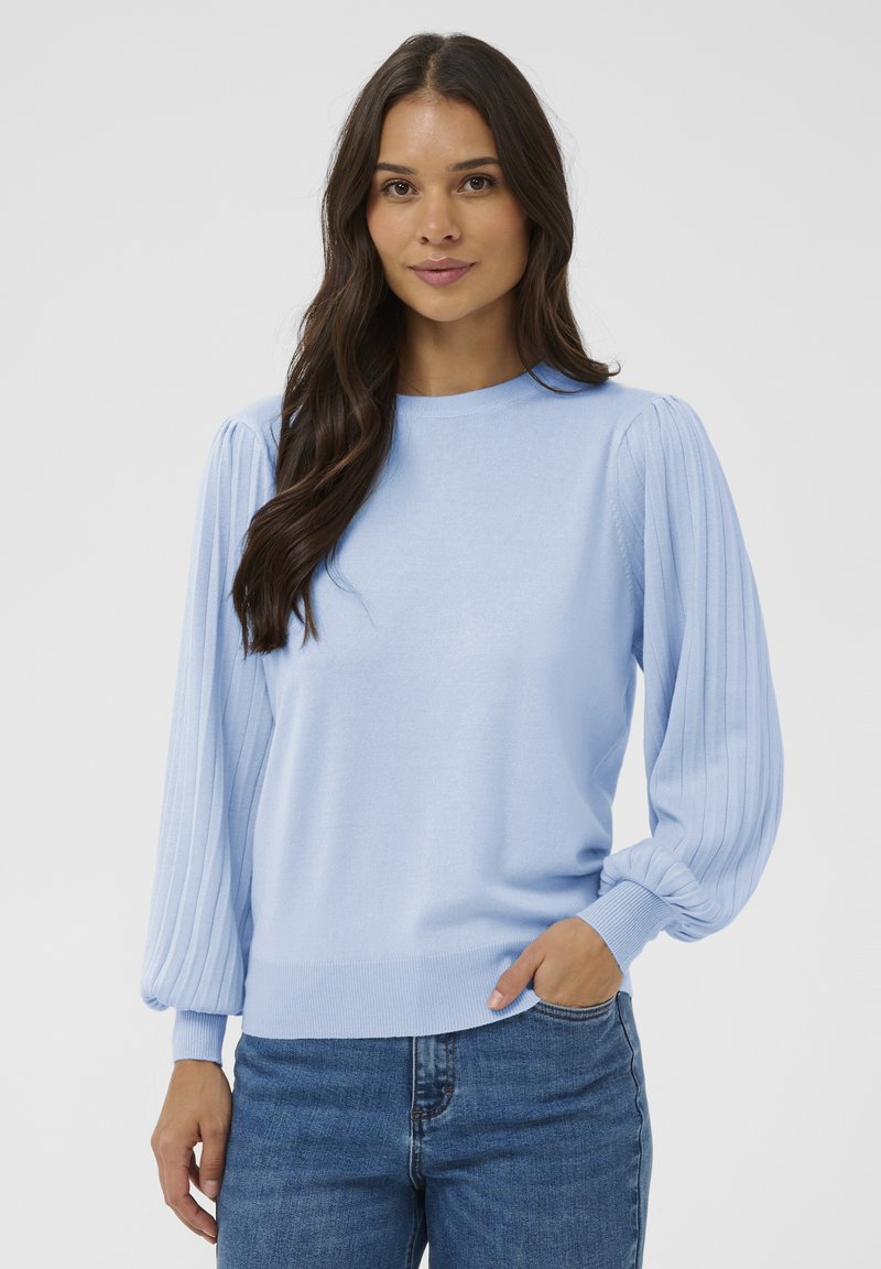 Hele sinine kampsun soonikkoes, volangidega pikad varrukad ja ümmargune kaelus; sile tekstuur ja istuv talje, sobitatud teksapükstega.