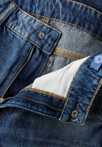 Jeans de denim con cremallera, costuras en color cobre y forro de bolsillo de tela blanca. El diseño incluye un botón de metal y detalles de cremallera.