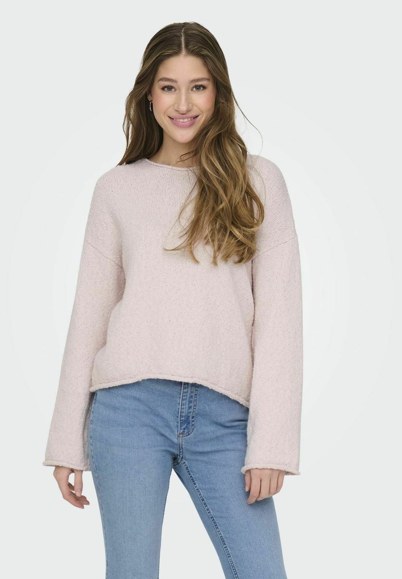 Pull en maille rose clair avec un col rond, des épaules tombantes et des manches longues. Il présente un ourlet légèrement court et une texture douce.