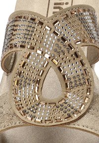 Sandalo open-toe con una tomaia texture dorata decorata con borchie metalliche, motivi geometrici e un design traforato decorativo.