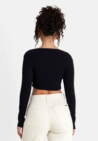 Schwarzes, gekürztes Langarmoberteil mit weitem Ausschnitt, kombiniert mit hellen, hochsitztenden Jeans mit aufgesetzten Taschen und dezenten Nähten.