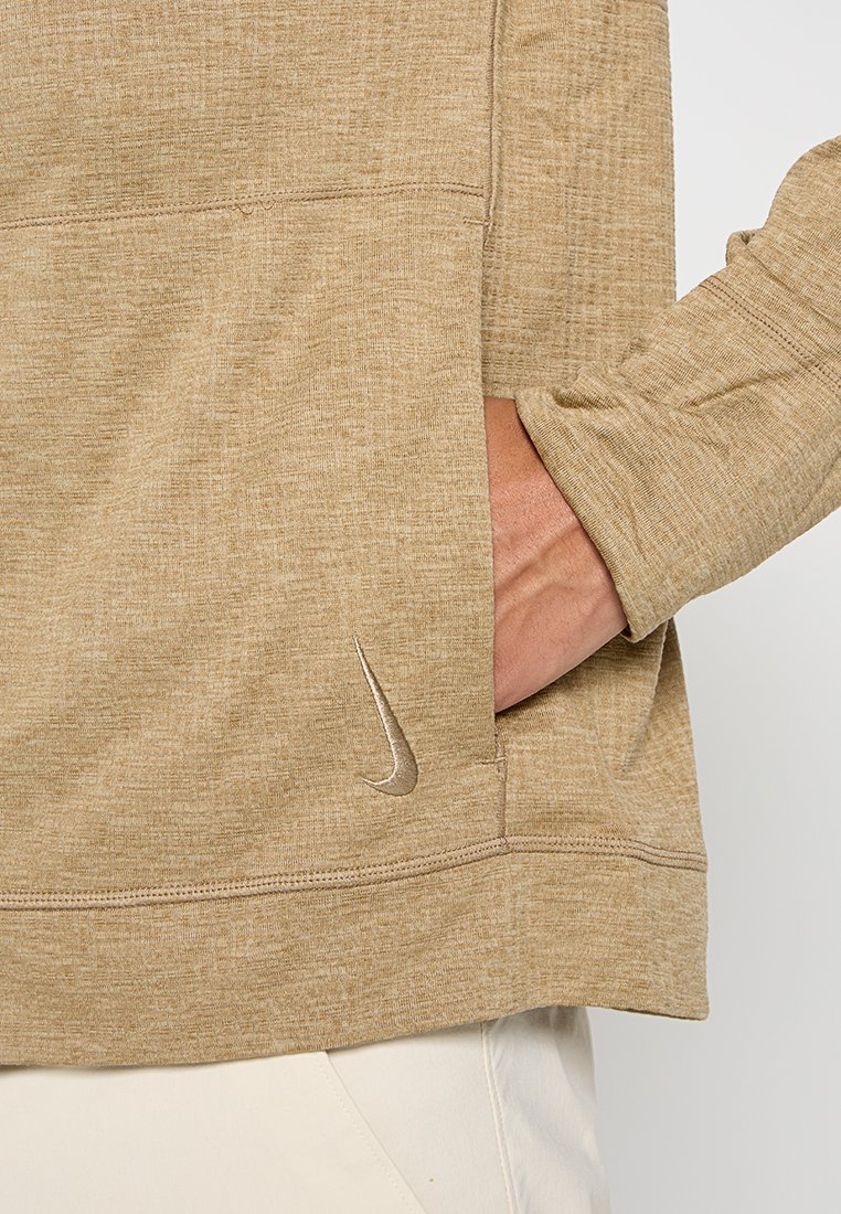 Mano nella tasca anteriore di una felpa beige Nike con il logo swoosh Nike visibile sul lato sinistro in basso.