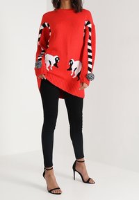 Maglione rosso lavorato a maglia con maniche a strisce bianche e nere, caratterizzato da due motivi di pecore bianche e particolari con pompon sui polsini.