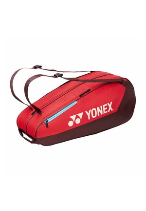 Bolsa deportiva Yonex roja y marrón con correas dobles para los hombros, bolsillo con cremallera azul y compartimento principal con cremallera, vista lateral en ángulo.