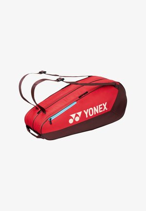 Bolsa deportiva Yonex roja y marrón con correas dobles para los hombros, bolsillo con cremallera azul y compartimento principal con cremallera, vista lateral en ángulo.