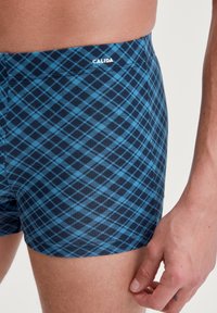 Boxers en plaid bleu et noir, fabriqués en matériau élastique, présentant un design ajusté avec un petit logo à la taille.