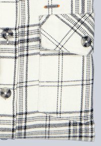 Weißes kariertes Flanellhemd mit schwarzen und blauen Linien. Verfügt über eine Brusttasche, rundliche schwarze Knöpfe und ein kleines Logoschild.