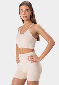 Sujetador deportivo beige y pantalones cortos de talle alto confeccionados con un tejido suave y texturizado; presenta un diseño fruncido en el sujetador y detalles acanalados en los pantalones cortos.