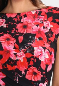 Tissu noir avec un motif floral rouge vif, rose et blanc comprenant de grandes fleurs et des feuilles sur un débardeur.