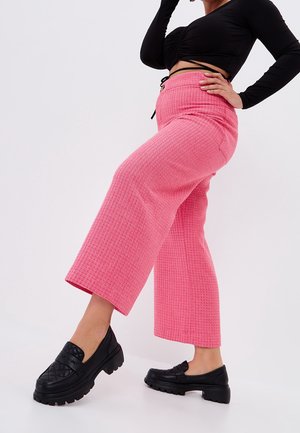 Pantalon large rose texturé avec une taille haute et un détail lacé. Assorti à des mocassins noirs épais avec un motif matelassé.
