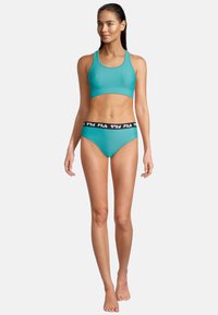 Türkiser Sport-BH und passender Bikini-Hose. Der BH hat ein schlichtes Design, während die Hose ein kontrastierendes schwarzes Elastikband mit Logo aufweist.