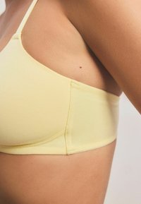 Sutien din țesătură galbenă cu o textură netedă. Dispune de bretele ajustabile și un design fără cusături pentru confort și adaptare.