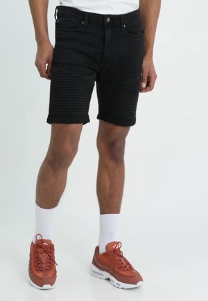 Sort denimshorts med ribbet detalj på benene, opsmøgede kanter, kombineret med røde sneakers og hvide sokker.