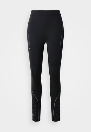 Black leggings with a high waistband, featuring silver accent stitching, side pockets, and dotted perforations along the lower legs.