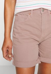 Shorts de mezclilla rosa claro con dobladillo enrollado, que cuentan con dos bolsillos frontales y detalles de costura sutiles, combinados con una blusa de rayas multicolores.