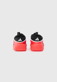 Une paire de chaussures de sport rouges et noires vues de l'arrière, avec des logos de marque blancs sur les cols de talon et des semelles texturées.