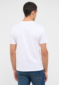 Biała bawełniana koszulka z krótkim rękawem i okrągłym dekoltem, zestawiona z niebieskimi dżinsami z dwoma tylnymi kieszeniami i ozdobnymi przeszyciami.