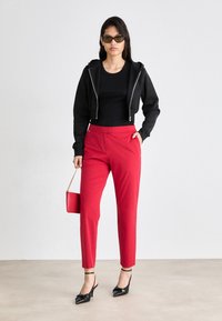 Juodas trumpas prailgintas megztinis, prigludęs juodas marškinėlis, raudonos pritaikytos kelnės, juodi kulniukai ir mažas raudonas rankinės. Lygi tekstūra, elegantiškas dizainas.