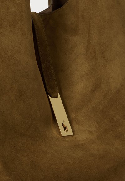 Brūns zamšs tote maisiņš ar gludu zeltītu aksesuāru un logotipa detaļu. Tekstūra ir mīksta un samtaini.