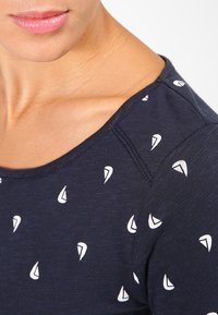 T-shirt bleu marine avec un col rond, ornée de petits motifs de voiliers blancs. Fabriqué dans un tissu doux et texturé.
