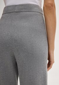 Grijze gebreide broek met een brede tailleband, van een gladde, gestructureerde stof en minimale naaddetails, gezien vanaf de achterkant.