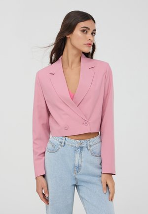 Blazer rosa cropped con design a doppio bottone e rever a scollo, abbinato a jeans azzurri chiari con decorazioni sottili.