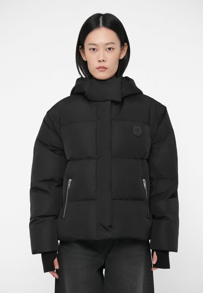 Doudoune noire au design boxy, avec des poches latérales zippées et un col montant. Texture douce avec un logo bien visible sur la poitrine.
