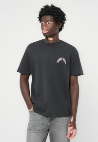 Sort bomulds t-shirt med rund hals, korte ærmer og pink "Tommy Jeans" logo på brystet; parret med grå jeans.
