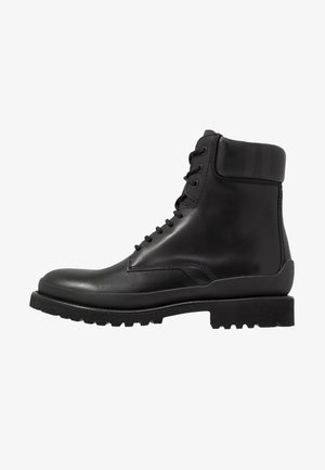 Bottine noire en cuir avec laçage à l'avant, col rembourré et semelle épaisse en caoutchouc rainurée pour adhérence et durabilité.