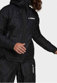 Sort isoleret jakke med lynlåslukning, quiltet design og høj krave. Har Terrex-logo på brystet og armen.