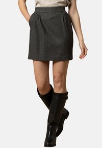 Gonna grigia plissettata con vita alta, realizzata in tessuto testurizzato con sottili righe verticali, abbinata a stivali neri al ginocchio.