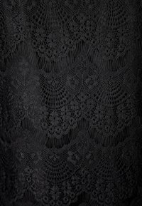 Svart spets tyg med intrikata blommönster och geometriska mönster. Texturen är delikat, med synliga upphöjda trådar och detaljer.