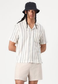 Korte mouwen, knoopsluiting overhemd met horizontale marineblauwe en crèmekleurige strepen; enkele borstzak; gecombineerd met licht beige shorts; comfortabele pasvorm.