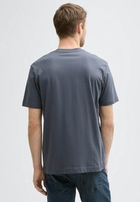 Camiseta de algodón gris con mangas cortas, escote redondo y corte relajado, vista desde la parte de atrás. Sin logotipos ni patrones visibles.
