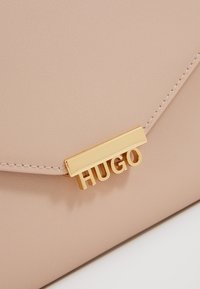 Růžová syntetická kabelka s texturovaným povrchem, zdobená zlatým zapínáním s logem "HUGO" a pečlivým prošitím.