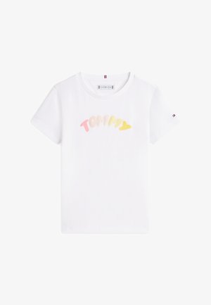T-shirt blanc à manches courtes avec le texte "TOMMY" en pastel rose, beige et jaune sur la poitrine, et un petit logo drapeau sur la manche droite.