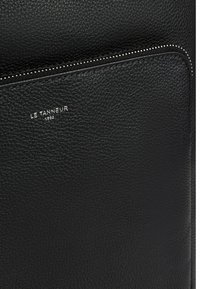 Borsa in pelle nera con superficie testurizzata, dotata di chiusura con zip e tasca frontale. Nome del marchio in rilievo argento "Le Tanneur 1898."