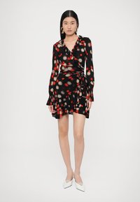 Μαύρο κρουαζέ φόρεμα με κόκκινες και μπεζ πουά, βολάν στο κάτω μέρος, μακριά μανίκια και δέσιμο στη μέση, κατασκευασμένο από ελαφρύ ύφασμα.