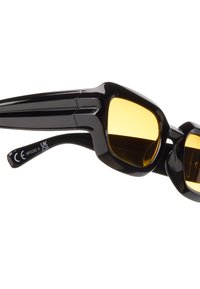 Svarta solglasögon med kantiga bågar, gula linser och texturerade sidor. På armen finns märkning och certifieringsdetaljer.