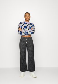 Suéter de malha xadrez de várias cores com um design cropped, combinado com calças pretas de cintura alta em flare, com uma textura ondulada e fecho de botão.