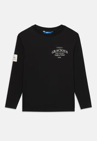 Sort langærmet T-shirt med rund halsudskæring, hvid tekst "GRACIOUS" og lille mærke på venstre ærme, præsenteret mod hvid baggrund.
