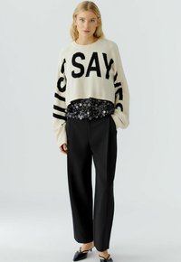 Cream sweater with "JUST SAY YES" in black, layered over a black sequined top; paired with tailored black pants and pointed black shoes.